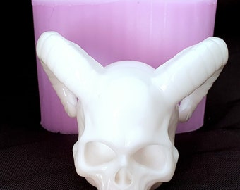 May include: White resin skull with horns, sitting on a pink silicone mold. The skull has detailed features, including eye sockets, a nose, and a mouth.