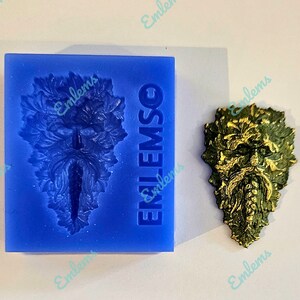 Peut inclure: Un moule en silicone bleu avec le mot "EMLSO" imprimé dessus. Le moule est en forme de visage d'homme vert avec des feuilles et des vignes. Une coulée en résine dorée de l'homme vert est présentée à côté du moule.