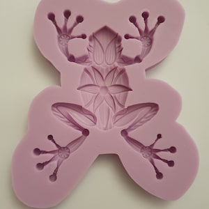 May include: Purple silicone mold shaped like a frog with a floral design on its back. The mold has detailed impressions for the frog's legs and toes.