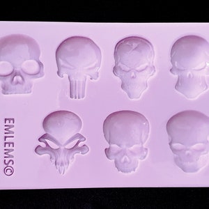 May include: A purple silicone mold with seven skull shapes. The mold is for making candy, chocolate, or other treats. The mold is labeled "EMLEMS©".
