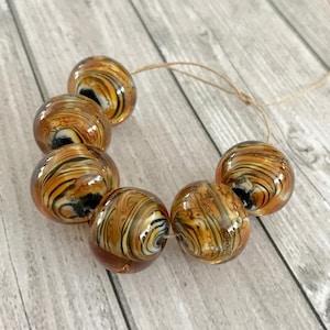 Peut inclure: Un brin de perles en verre brun, noir et blanc avec un motif tourbillonnant. Les perles sont enfilées sur un cordon de ficelle naturelle.