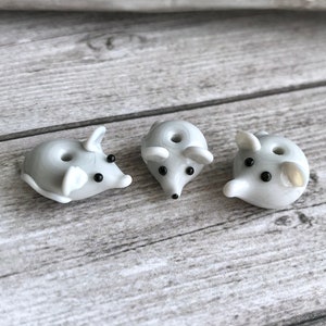 Op de afbeelding: Drie kleine, witte glazen muisjes met zwarte ogen. De muizen kijken naar voren met hun staarten eronder.
