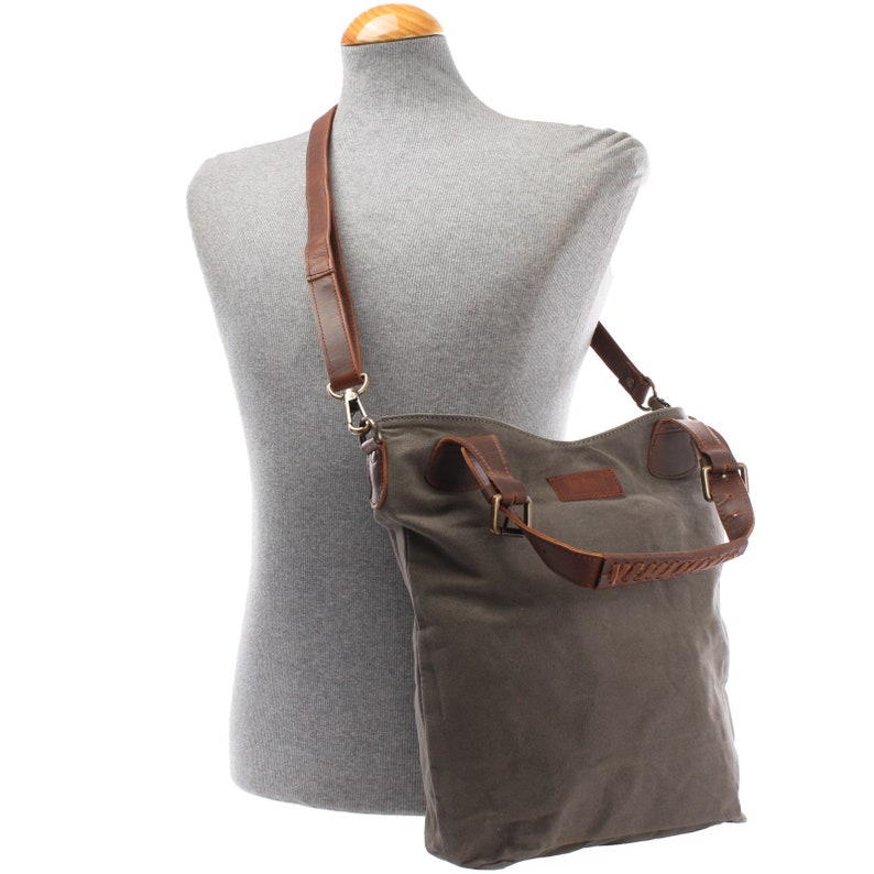 May include: A gray canvas tote bag with brown leather straps and accents. The bag has a long strap for carrying it over the shoulder.