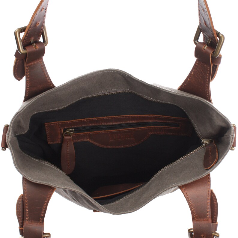 May include: A gray canvas tote bag with brown leather straps and buckles. The bag has a zippered pocket on the inside.