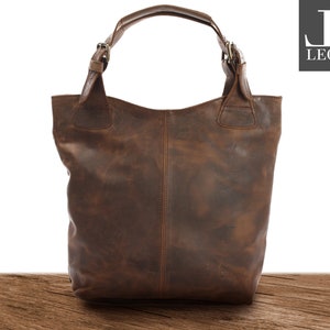 May include: A brown leather tote bag with a top handle and buckle closures. The bag has a distressed look and is made of high-quality leather.