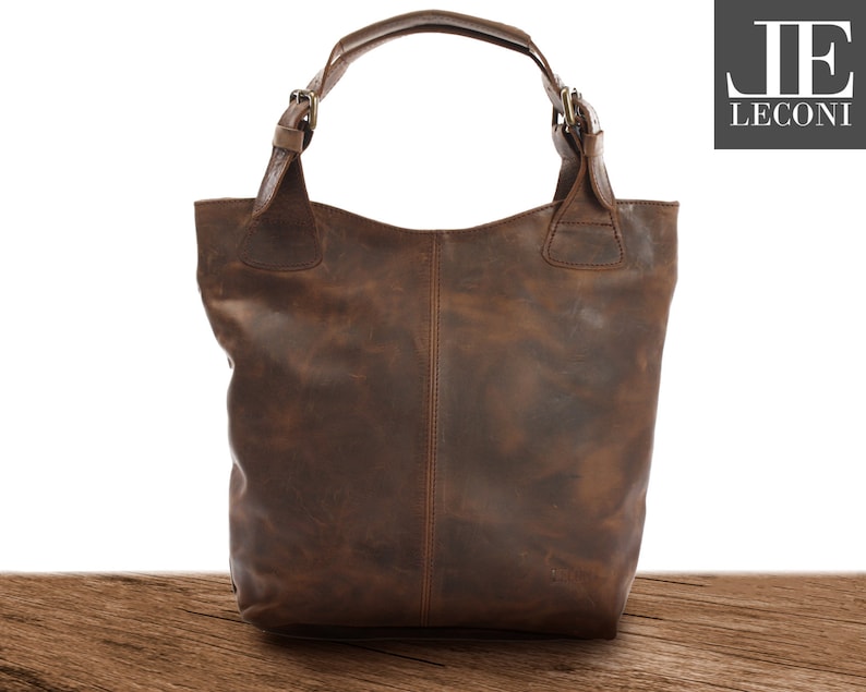 May include: A brown leather tote bag with a top handle and buckle closures. The bag has a distressed look and is made of high-quality leather.