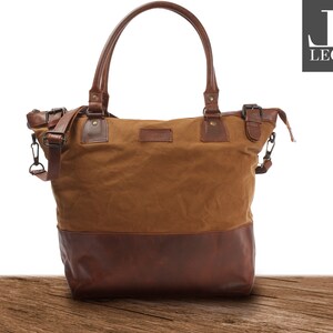 Könnte beinhalten: Eine braune Canvas- und Ledertasche mit einem braunen Lederriemen und einer Metallschnalle. Die Tasche hat einen braunen Lederboden und ein braunes Canvas-Oberteil.