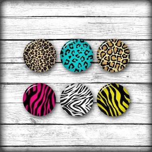May include: Six round, colorful buttons with different animal print patterns. The buttons are arranged in two rows of three. The buttons are on a white wood background.