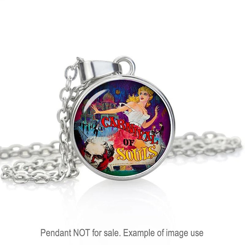Puede incluir: Collar de plata con un colgante redondo que presenta una ilustraci&oacute;n colorida de una mujer en un entorno de carnaval. El colgante tiene el texto "Carnival of Souls" impreso en &eacute;l.