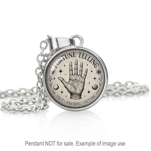 May include: A silver-toned pendant necklace featuring a circular glass cabochon with a black and white illustration of a palmistry hand. The text FORTUNE TELLING is printed at the top, with PAST, PRESENT, FUTURE at the bottom, surrounded by stars and moons.