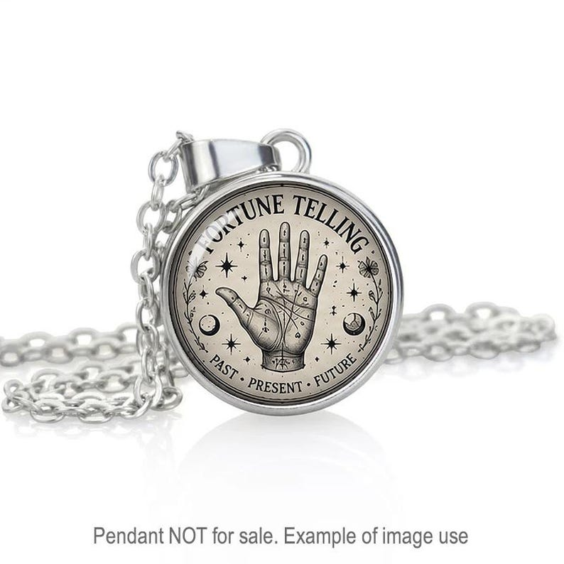 May include: A silver-toned pendant necklace featuring a circular glass cabochon with a black and white illustration of a palmistry hand. The text FORTUNE TELLING is printed at the top, with PAST, PRESENT, FUTURE at the bottom, surrounded by stars and moons.