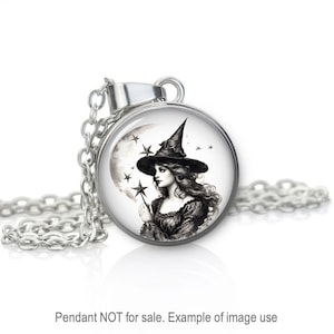 May include: A silver necklace with a round glass pendant featuring a black and white illustration of a witch with a pointed hat, holding a wand in front of a crescent moon and stars.