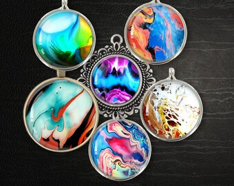 Könnte beinhalten: Sechs runde Anhänger mit silbernem Rahmen und farbenfrohen, abstrakten Fluid-Art-Designs. Die Anhänger sind in einem Kreis um einen größeren, verzierten silbernen Anhänger angeordnet. Der Text "Fluid Designs" ist unter den Anhängern sichtbar.