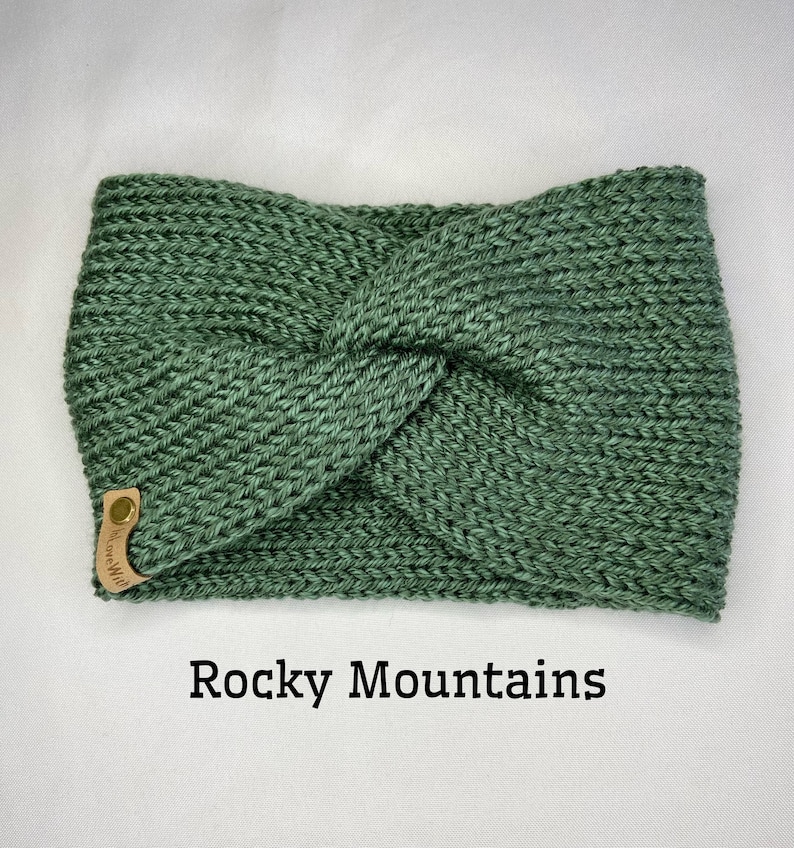 May include: A green knitted headband with a knotted design. The headband has a small leather tag with the text "Rocky Mountains" on it.