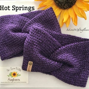 May include: Purple knitted headband with a twisted knot design. The headband is handmade and has a small brown leather tag with the text "In Love With" on it.