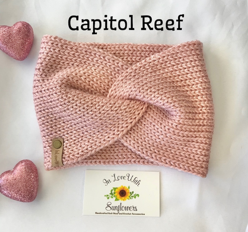 May include: A pink knitted headband with a knotted design. The headband has a brown leather tag with the text "In Love With Sunflowers" on it. The text "Capitol Reef" is written in black above the headband.