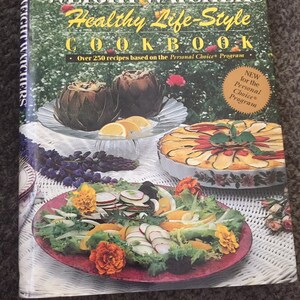 May include: A Weight Watchers cookbook with a green background and a photo of a salad on the front cover. The title of the book is "Weight Watchers Healthy Life-Style Cookbook" and the text "Over 250 recipes based on the Personal Choice Program" is also visible. A sticker on the cover reads "New for the Personal Choice Program".