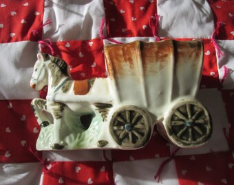 May include: A white ceramic figurine of a horse-drawn wagon. The wagon has a brown roof and wheels. The horse is brown and white.