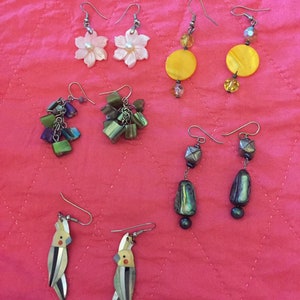 May include: Assortment of earrings featuring various designs, including flowers, geometric shapes, and birds. The earrings are made of different materials, such as metal, beads, and shells.