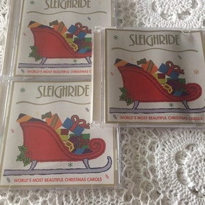 May include: Three CD cases with a red sleigh filled with presents and the text "Sleighride" and "World's Most Beautiful Christmas Carols" on the front.