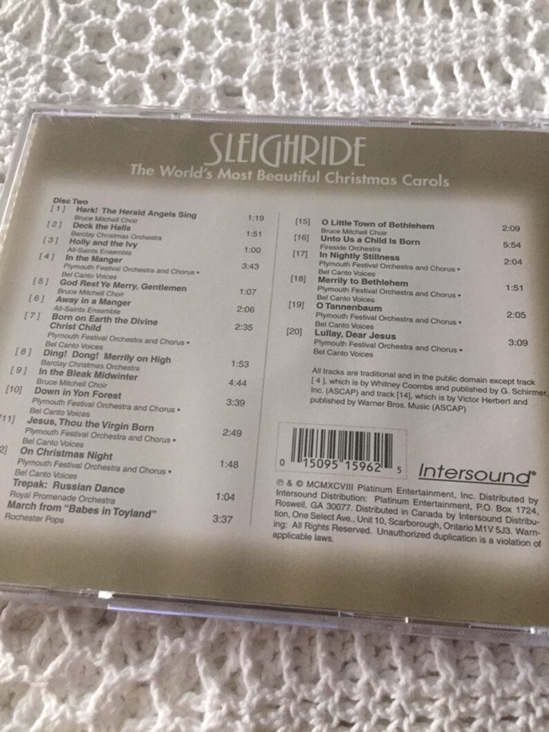 May include: The back of a CD case for a Christmas music compilation titled "Sleighride: The World's Most Beautiful Christmas Carols". The case features a list of songs and artists, including "Hark! The Herald Angels Sing" by Bruce Mitchell Choir, "Deck the Halls" by Barclay Christmas Orchestra, and "O Little Town of Bethlehem" by Bruce Mitchell Choir. The case also includes a barcode and copyright information.