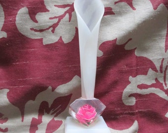 May include: White plastic vase with a single pink flower in a clear plastic base. The vase is shaped like a calla lily.