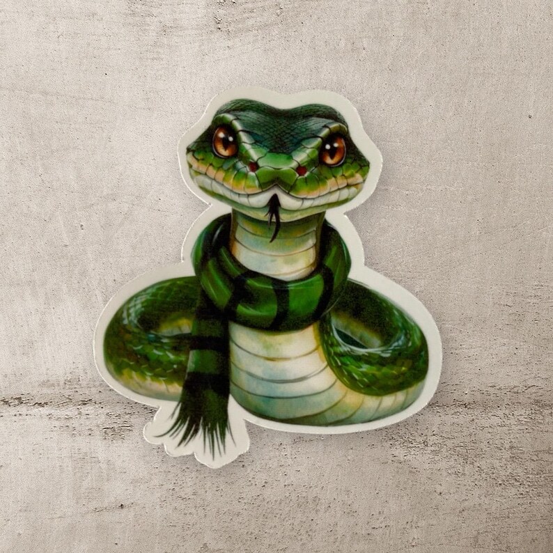May include: A green snake with a green scarf wrapped around its neck. The snake has a sly expression on its face.