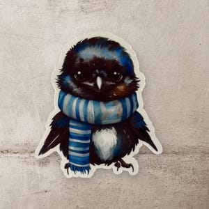 May include: A black and blue bird wearing a blue and white striped scarf. The bird has a white chest and is looking down.
