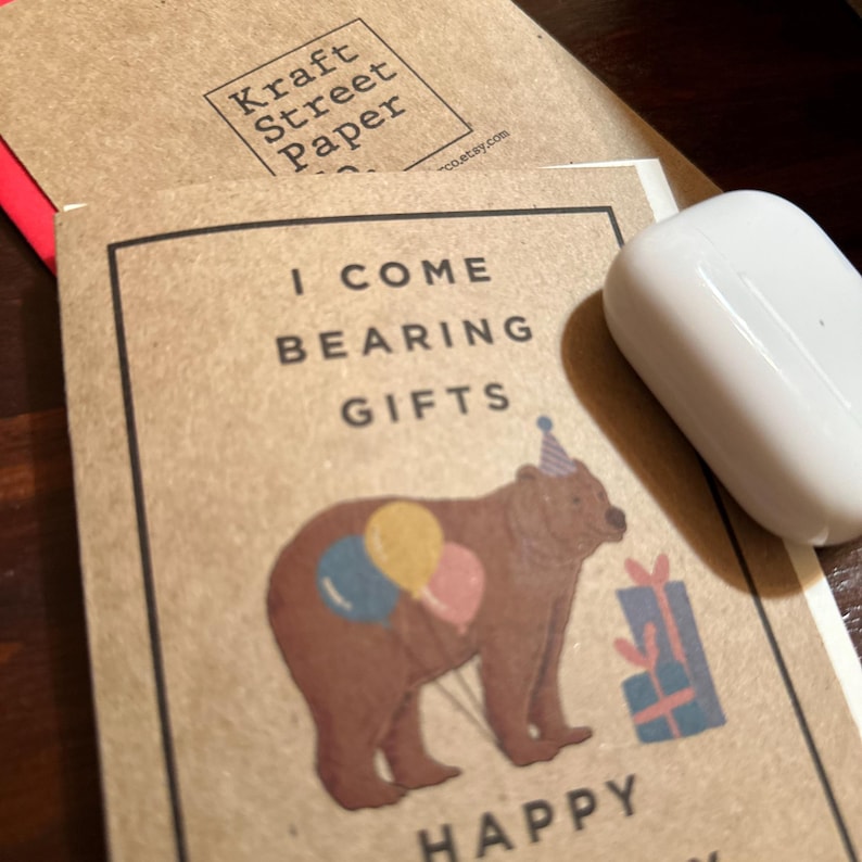 May include: A brown bear wearing a party hat holds balloons and a gift box. The card reads "I come bearing gifts" and "Happy Birthday".
