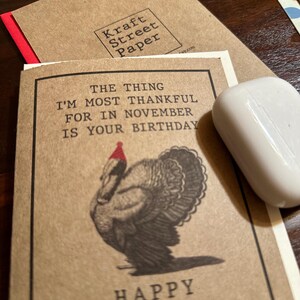 May include: A brown card with a turkey wearing a red Santa hat. The card says "The thing I'm most thankful for in November is your birthday." and "Happy".