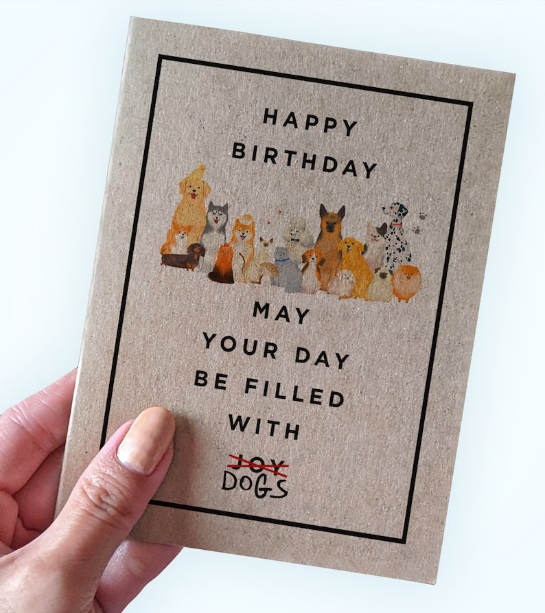 May include: A brown card with a black border and the text "Happy Birthday" at the top. A group of dogs are illustrated in the middle of the card. The text "May your day be filled with Joy Dogs" is at the bottom of the card. The word "Joy" is crossed out and the word "Dogs" is written below it.