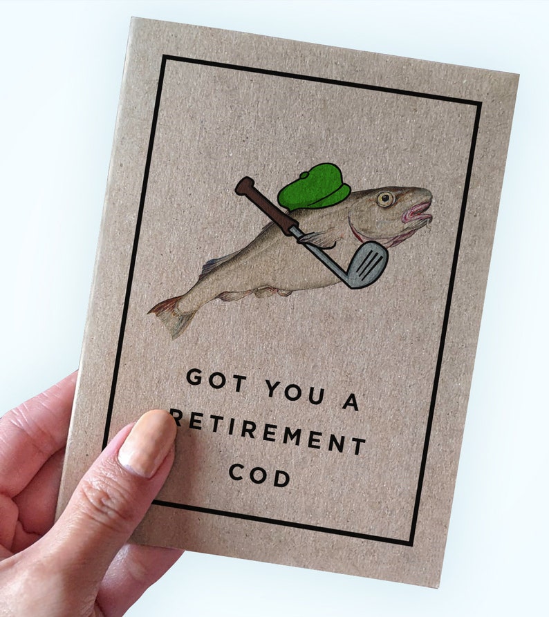 Pu&ograve; includere: Un biglietto marrone con un'illustrazione di un pesce di cartone animato che indossa un cappello da golf verde e tiene un bastone da golf. Il testo sul biglietto dice "GOT YOU A RETIREMENT COD".