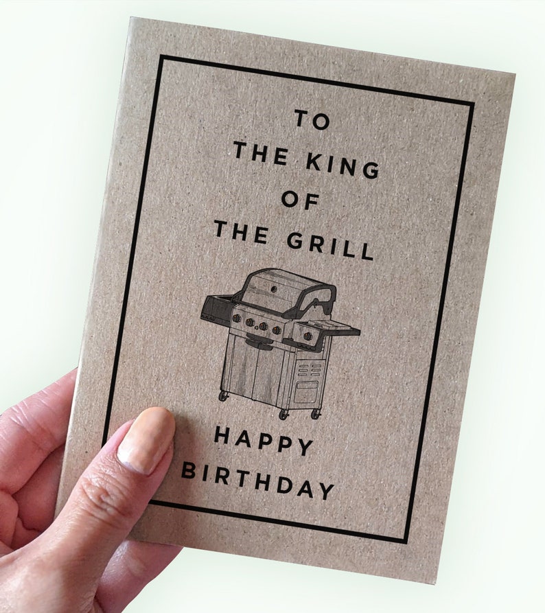May include: A brown card with black text and a black and white illustration of a grill. The text reads "To the King of the Grill Happy Birthday".