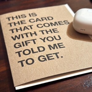 Może przedstawiać: Brązowa karta z białym tekstem, kt&oacute;ry brzmi "THIS IS THE CARD THAT COMES WITH THE GIFT YOU TOLD ME TO GET."