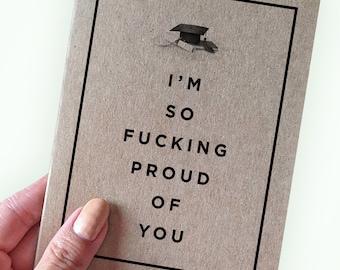 May include: A brown card with a black border and a graduation cap illustration. The text on the card reads "I'm so fucking proud of you."
