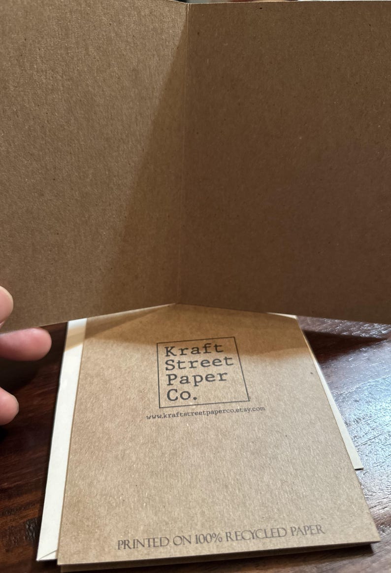 K&ouml;nnte beinhalten: Eine braune Karte mit dem Text "Kraft Street Paper Co." und der Website-Adresse "www.kraftstreetpaperco.etsy.com". Die Karte tr&auml;gt au&szlig;erdem den Text "Gedruckt auf 100% Recyclingpapier".