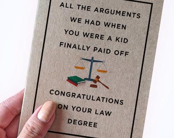 Può includere: Un biglietto marrone con testo nero che recita "Tutti gli argomenti che abbiamo avuto quando eri bambino hanno finalmente dato i loro frutti." C'è un disegno di una bilancia con libri e un martello. Il testo "Congratulazioni per la tua laurea in giurisprudenza" è anche sul biglietto.