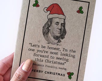 May include: A Christmas card featuring a portrait of Benjamin Franklin wearing a Santa hat. The card has the text "Let's be honest, I'm the one you're most looking forward to seeing this Christmas" and "Merry Christmas."
