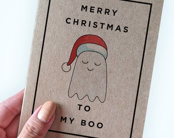 Op de afbeelding: Een bruine kaart met een zwarte rand en de tekst "Merry Christmas to my Boo". Een cartoon-spook met een kerstmanmuts staat in het midden van de kaart.