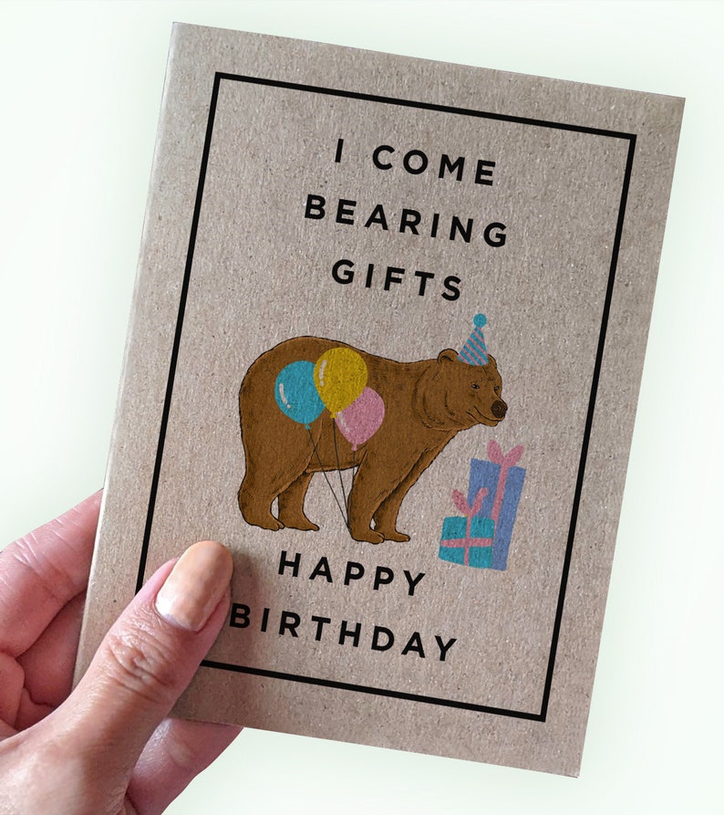 May include: A brown bear wearing a party hat and holding balloons and presents. The text on the card reads "I come bearing gifts Happy Birthday".