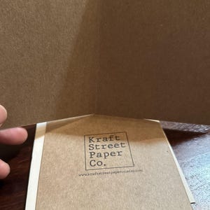 May include: A folded card with a brown paper exterior. The back of the card has a logo that reads "Kraft Street Paper Co." and the website address "www.kraftstreetpaperco.etsy.com". The bottom of the card reads "Printed on 100% Recycled Paper".