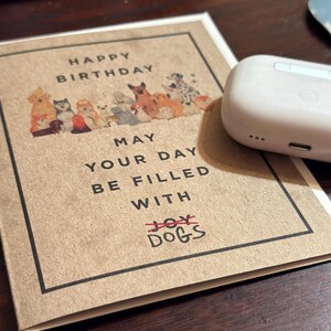 May include: A brown card with a happy birthday message and a picture of dogs. The card says "May your day be filled with dogs" with the word "joy" crossed out.