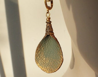Pode incluir: Brincos de couro verde e dourado com um design de metal dourado detalhado. Os brincos estão pendurados na orelha de um manequim. O texto "luisi misi schmuckmanufaktur" é visível na parte inferior da imagem.