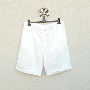 May include: White shorts hanging on a black hanger. The shorts have a button closure and pockets. A small logo is visible on the left leg. The shorts are made of a lightweight material, perfect for warm weather.
