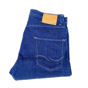 May include: A pair of dark blue denim jeans with a brown leather patch on the back waistband that says "Sugar Cane & Co."