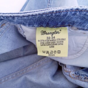 May include: A light blue denim jean label with the Wrangler logo and the text "32-34" and care instructions. The label also includes the text "97% Cotton, 3% Elastane".