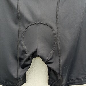 Puede incluir: Pantalones cortos de ciclismo negros con una inserci&oacute;n acolchada central con costuras en zigzag visibles a lo largo de los bordes. La prenda est&aacute; confeccionada con un tejido liso y el&aacute;stico con costuras reforzadas que recorren verticalmente los paneles frontales.