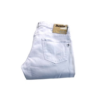 May include: White denim jeans, folded neatly. The jeans feature a back pocket with a small cross and a brown leather tag with "Paciotti" and "40 US".