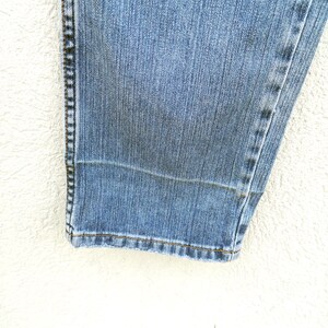 May include: Close-up of the bottom hem of a pair of blue denim jeans. The hem is folded and stitched with a dark thread.