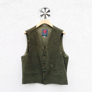 Op de afbeelding: Olijfgroene vest met een V-hals, knoopsluiting en twee voorzakken. Het vest heeft een klein geborduurd embleem rechtsonder en een label met een rood embleem aan de binnenkant. Het hangt aan een houten hanger.